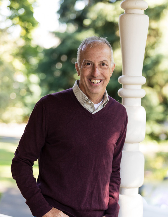 white professional business man in burgundy sweater leaning against a porch pillar