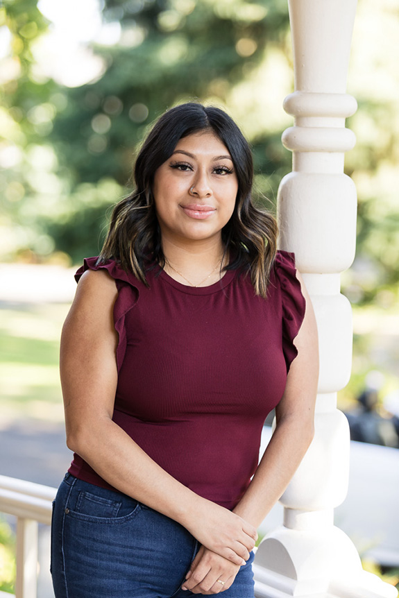 hispanic professional business woman in a burgundy top and jeans leaning against a porch pillar